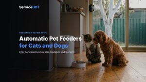 A tabby cat and a red Cavoodle waiting beside an automatic pet feeder on a kitchen floor