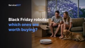 A couple on a couch and their golden retriever watch a white robot vacuum clean the timber floor, next to an opened delivery box.