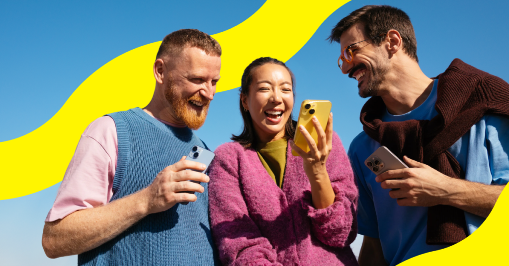 Three friends outdoors laughing as they check their phones
